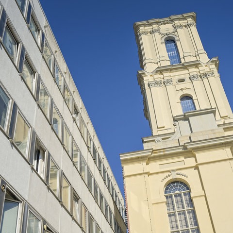 Ein Kirchturm neben einem modernen Bürogebäude