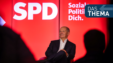 Bundeskanzler Olaf Scholz sitzt bei einer Veranstaltung vor einem SPD-Logo auf der Bühne