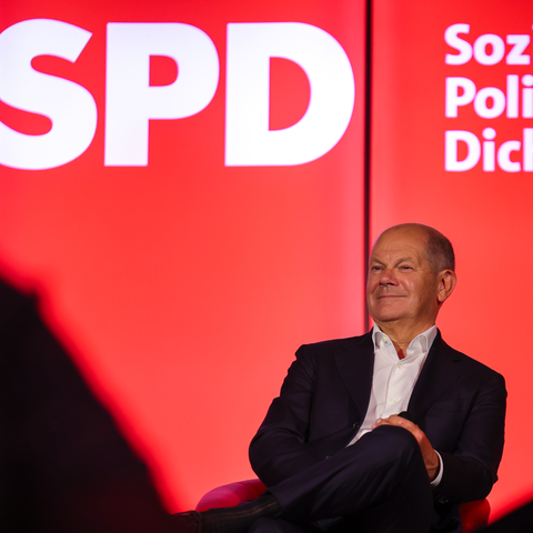 Bundeskanzler Olaf Scholz sitzt bei einer Veranstaltung vor einem SPD-Logo auf der Bühne