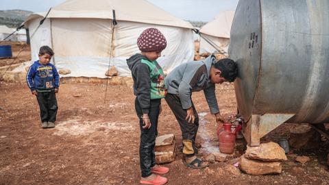 Syrische Kinder füllen Wasser aus einem Tank in eine Kanne in einem Flüchtlingslager für Binnenflüchtlinge in der Nähe des Dorfes Kafr Aruq.