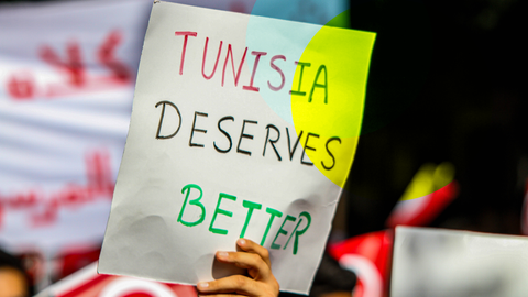 Ein Mensch hält ein Schild hoch, auf dem steht "Tunesia deserves better"