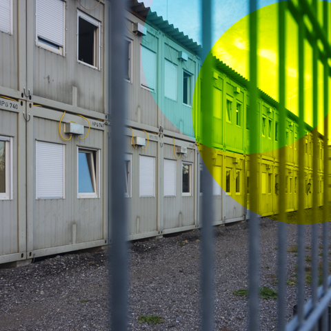 Eine Flüchtlingsunterkunft aus Wohncontainern die von einem hohen Zaun umgeben ist