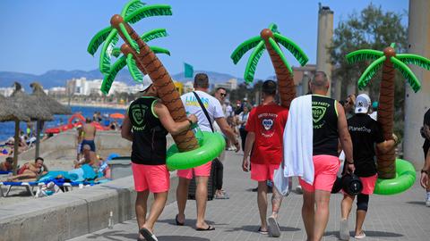 Männer tragen an einem sonnigen Tag Plastikpalmen am Strand Arenal.